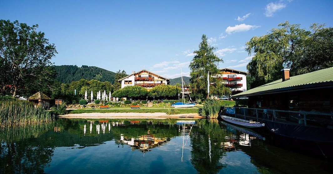 Hotel am Tegernsee mit Seeufer und Bergkulisse im Hintergrund.